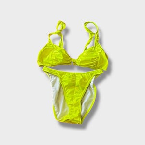 May include: A neon yellow bikini set. The top has twisted straps and a gathered bust. The bottoms are high-cut with white lining. The swimsuit is made of a shiny, lightweight material.