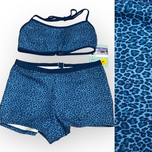 May include: A two-piece swimsuit set in a blue leopard print. The top is a halter style with a clasp closure, and the bottoms are boy shorts. The fabric has a dark blue trim. The set is displayed on a white background.