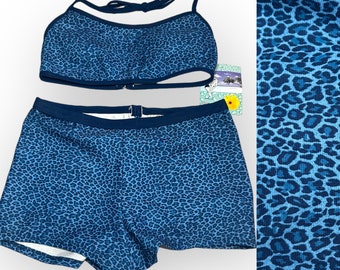 May include: A two-piece swimsuit set in a blue leopard print. The top is a halter style with a clasp closure, and the bottoms are boy shorts. The fabric has a dark blue trim. The set is displayed on a white background.