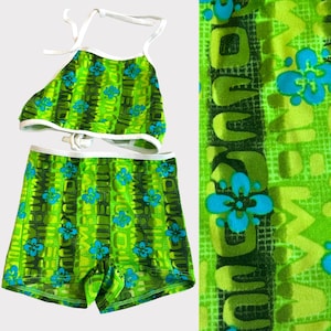 May include: Green and blue patterned swimsuit with a halter top and matching shorts. The pattern features a repeating design of flowers and the word "Hawaii".