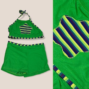 May include: Green two-piece swimsuit with a halter top and shorts. The top has a star-shaped patch with colorful stripes.
