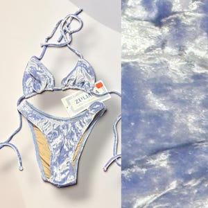May include: A light blue velvet bikini set with tie closures. The bikini top has triangle cups, and the bottoms are a classic cut. A tag with the brand name "Zuliana" is attached. The fabric has a soft, textured appearance.