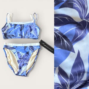 May include: Two-piece swimsuit set with a blue and white floral pattern. The top has thin straps and a square neckline. The bottoms are high-waisted. The tag reads "Expression".
