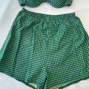 May include: A two-piece swimsuit set in a green and navy blue gingham pattern. The top is a halter-style bikini, and the bottoms are high-waisted shorts. The fabric has a soft, textured appearance. The set is designed for swimwear.