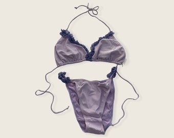 May include: A lavender-colored bikini with a halter top and a ruffled trim. The bikini is made of a ribbed fabric.