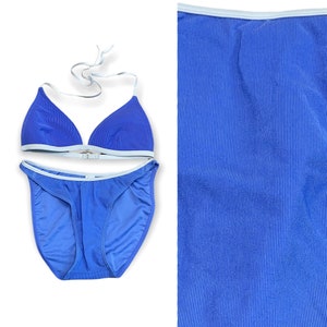 Puede incluir: Un bikini azul con ribetes blancos. La parte superior es de estilo triangular y la inferior es de estilo de corte alto.