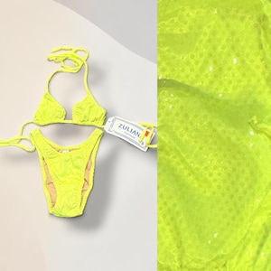 Könnte beinhalten: Neongelbes Bikini-Set mit einem Triangel-Oberteil und einem hoch geschnittenen Unterteil. Der Bikini hat ein strukturiertes Muster und wird mit einem Etikett mit der Aufschrift "ZULIAN, Swimwear" präsentiert. Das Set befindet sich auf hellem Hintergrund.