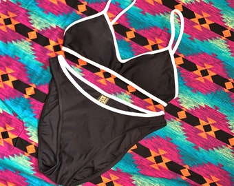 May include: Black bikini with white trim. The top is a triangle style and the bottom is a high-cut style.