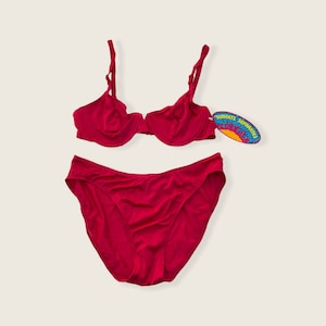 May include: A red two-piece swimsuit with a bra top and a bikini bottom. The bra top has underwire and adjustable straps. The bikini bottom has a high-cut leg. The swimsuit has a tag that says "Sunsets Separates".
