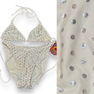 May include: White bikini with silver polka dots. The bikini top is a triangle style with adjustable straps. The bikini bottom is a high-cut style with a V-shaped front.