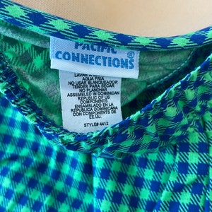 May include: Close-up of a garment with a blue and green checkered pattern. The garment has a blue trim and a tag that reads "PACIFIC CONNECTIONS". The tag also includes washing instructions and the style number 4412.