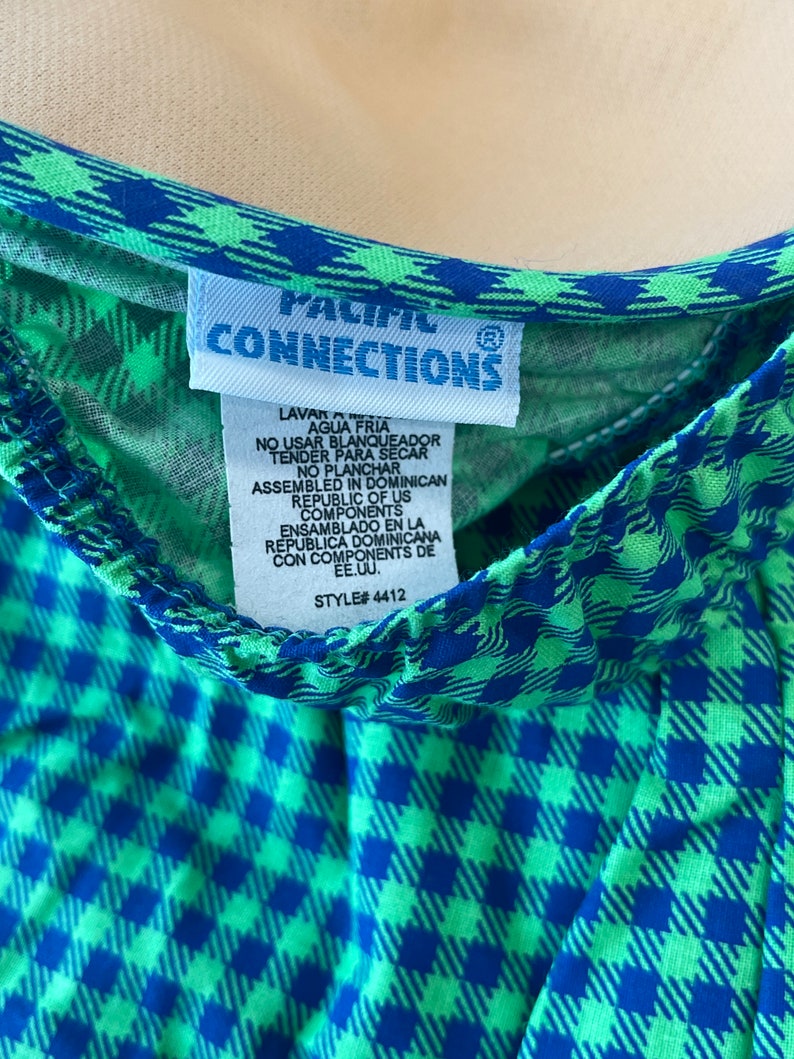 May include: Close-up of a garment with a blue and green checkered pattern. The garment has a blue trim and a tag that reads "PACIFIC CONNECTIONS". The tag also includes washing instructions and the style number 4412.