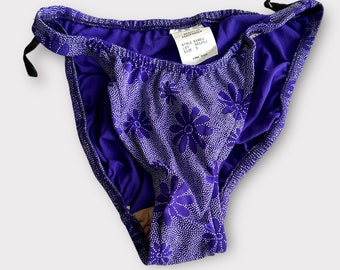 Könnte beinhalten: Lilafarbener Bikini-Slip mit weißem Blumenmuster und einem kleinen Etikett mit der Aufschrift "Style 8403, Lot 101, Größe S".