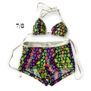 May include: A two-piece swimsuit with a floral print in shades of purple, green, yellow, and pink. The top is a triangle style with white straps. The bottom is a high-waisted, short style with a white waistband.