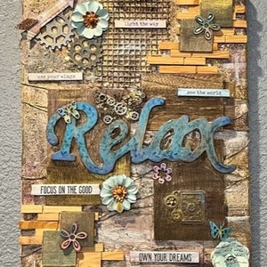 Op de afbeelding: Een mixed media canvas met een rustieke bruine achtergrond en verschillende texturen. Het woord "Relax" is geschreven in blauwe en metalen letters. Het canvas is versierd met tandwielen, bloemen en andere versieringen. De tekst "use your wings", "light the way", "see the world", "focus on the good" en "own your dreams" is ook inbegrepen.