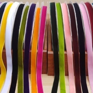 Op de afbeelding: Assortiment van 18 spoelen met fluwelen lint in verschillende kleuren, waaronder teal, paars, geel, wit, groen, donkerpaars, oranje, roze, lichtroze, bordeaux, zwart en lichtblauw.