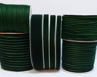 May include: Four spools of dark green velvet ribbon. The ribbon is wound around spools with white cardboard centers.