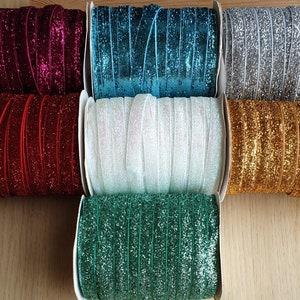 Puede incluir: Surtido de siete carretes de cinta de brillo en varios colores, incluyendo rojo, blanco, dorado, plateado, azul verdoso y verde.