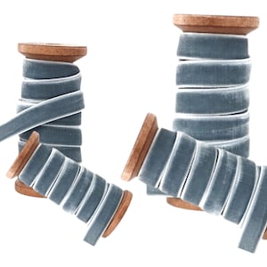 May include: Two spools of light blue velvet ribbon wound around wooden spools. The ribbon is approximately 1.2 cm wide.