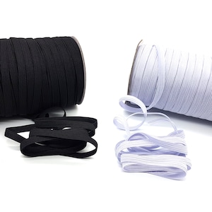 Puede incluir: Dos carretes de cordón elástico, uno negro y uno blanco, con unos centímetros de cada color desenrollados. El cordón elástico es un material común utilizado para coser y manualidades.