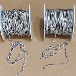 Peut inclure: Deux bobines de chaîne argentée, chacune avec une longueur de chaîne qui pend de la bobine. La chaîne est fine, délicate et torsadée.