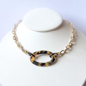 May include: A gold chain necklace with a large oval pendant made of brown and black tortoiseshell-patterned resin.