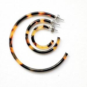 May include: Three tortoise shell hoop earrings of different sizes. The earrings are made of a brown and yellow patterned plastic.