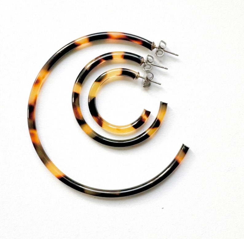 May include: Three tortoise shell hoop earrings of different sizes. The earrings are made of a brown and yellow patterned plastic.