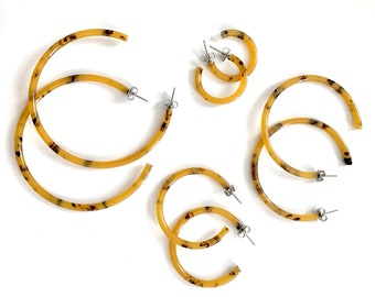 May include: Set of four tortoise shell hoop earrings in different sizes. The earrings are made of a brown and yellow plastic material with a mottled pattern.