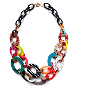 May include: A statement necklace featuring a multi-layered design of interlocking oval links in various colors and patterns, including solid black, bright red, neon green, turquoise, tortoise shell, white with black stripes, and a fine grid pattern.