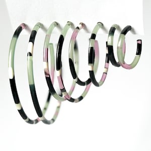 Peut inclure: Ensemble de cinq boucles d'oreilles créoles avec un motif géométrique en noir, blanc et vert. Les créoles sont en matériau translucide et ont une finition légèrement irisée.