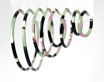May include: Set of five hoop earrings with a geometric pattern in black, white, and green. The hoops are made of a translucent material and have a slightly iridescent finish.