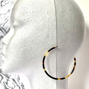 May include: A pair of large hoop earrings with a tortoiseshell pattern. The earrings are made of a brown and cream colored material.