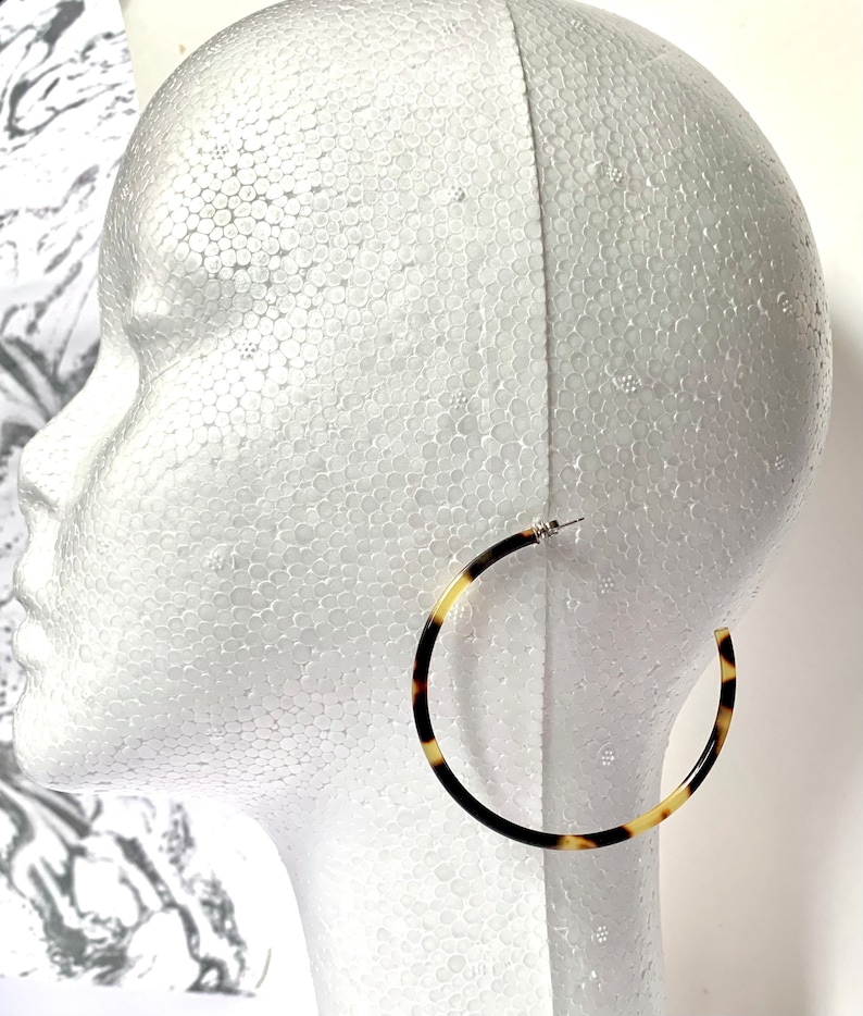 May include: A pair of large hoop earrings with a tortoiseshell pattern. The earrings are made of a brown and cream colored material.
