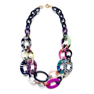 May include: A chunky statement necklace featuring a series of interlocking oval links in various colors and patterns, including solid black, bright magenta, zebra print, tortoiseshell, and translucent marbled acrylic, finished with a gold-tone clasp.