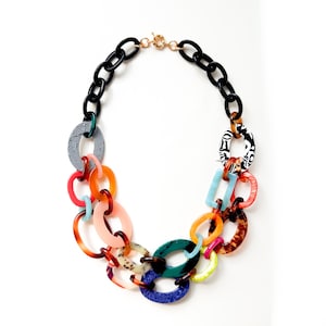 Può includere: Una colorata collana a catena con una miscela di maglie ovali e rettangolari in vari colori e motivi. La collana include maglie nere, blu, rosa, arancioni e verdi, con una chiusura dorata. Il design è audace e accattivante.