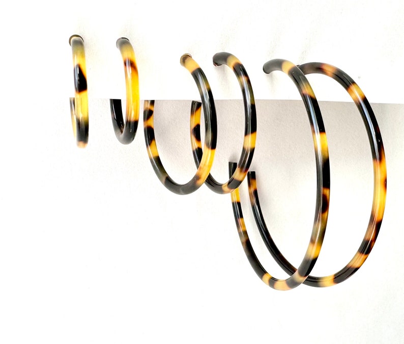 May include: Set of four tortoise shell hoop earrings in different sizes. The earrings are made of a brown and yellow plastic material with a mottled pattern.