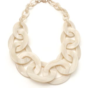 Könnte beinhalten: Cremefarbene Statement-Halskette mit großen, ovalen Gliedern. Das klobige Kettendesign ist mit einem zarten, goldfarbenen Verschluss verbunden. Die Halskette besteht aus einem marmorierten, cremefarbenen Material und ist ein auffälliges Accessoire.