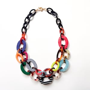 May include: A multi-colored statement necklace featuring interlocking oval links in various patterns and solid colors, including black, red, blue, green, orange, and yellow, connected by a gold-toned metal clasp at the top of the chain.