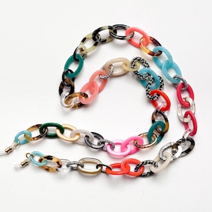 May include: A colorful eyeglass chain featuring oval links in various colors, including pink, blue, green, and tortoiseshell patterns. The chain has silver-colored connectors and is designed to hold eyeglasses.