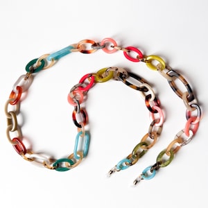 May include: A long eyeglass chain constructed from interlocking oval links in a variety of colors including translucent pink, bright red, lime green, teal, and tortoiseshell patterns, featuring small clear rubber loops at both ends for attachment.