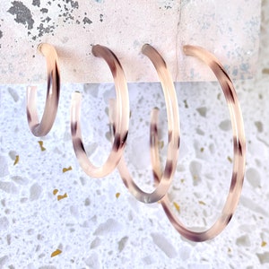 May include: Three pairs of tortoiseshell hoop earrings of varying sizes. The earrings are made of a translucent plastic material with a brown and white pattern.