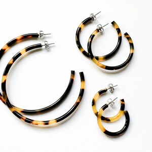 May include: Three pairs of tortoise shell hoop earrings of varying sizes. The earrings are made of a brown and yellow plastic material and have a shiny finish.