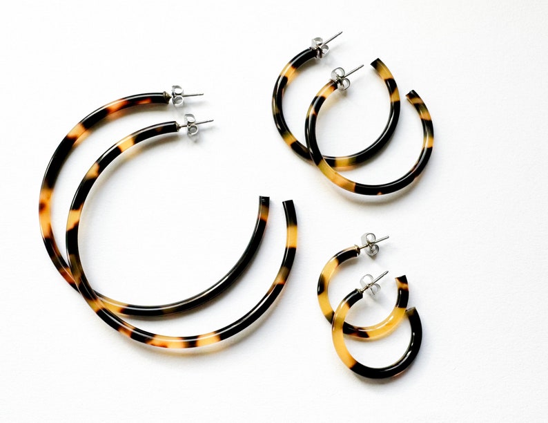 May include: Three pairs of tortoise shell hoop earrings of varying sizes. The earrings are made of a brown and yellow plastic material and have a shiny finish.