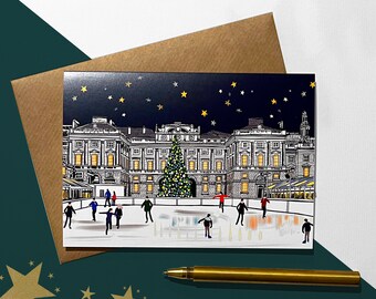 May include: A Christmas card featuring a black and white illustration of a building with a large Christmas tree in front of it. People are ice skating in front of the tree. The sky is dark blue with white stars.