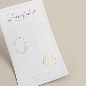 May include: A white certificate with a gold seal and the text "Zertifikat" in cursive. The certificate is for a lost tooth and includes a diagram of a mouth with teeth, a section for the child's name, date, and lost tooth details, and a section for the dentist's signature.