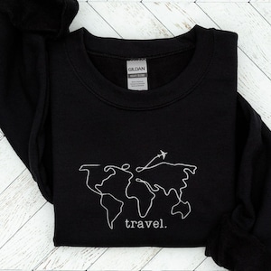 Puede incluir: Sudadera negra con un contorno blanco de un mapa del mundo y un avi&oacute;n. La palabra "travel" est&aacute; escrita debajo. La sudadera est&aacute; hecha de un material suave y tiene cuello redondo.
