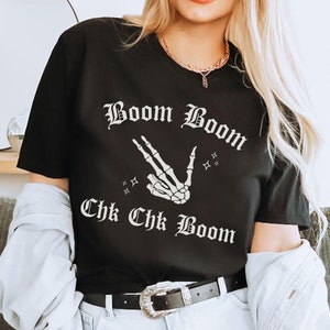 May include: Black t-shirt with a white skeleton hand making a peace sign and the text "Boom Boom Chk Chk Boom" in a gothic font.