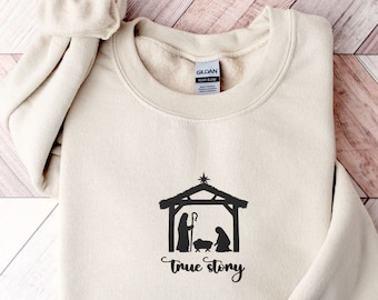 Pode incluir: Uma camisa de moletom bege com uma silhueta preta da cena da natividade e o texto "true story".