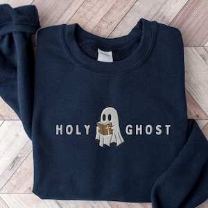 May include: A navy blue sweatshirt with a white ghost holding a book with a cross on it. The text "HOLY GHOST" is embroidered in white below the ghost.
